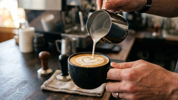 Barista toarnă lapte spumat într-o ceașcă de cafea pentru latte art.